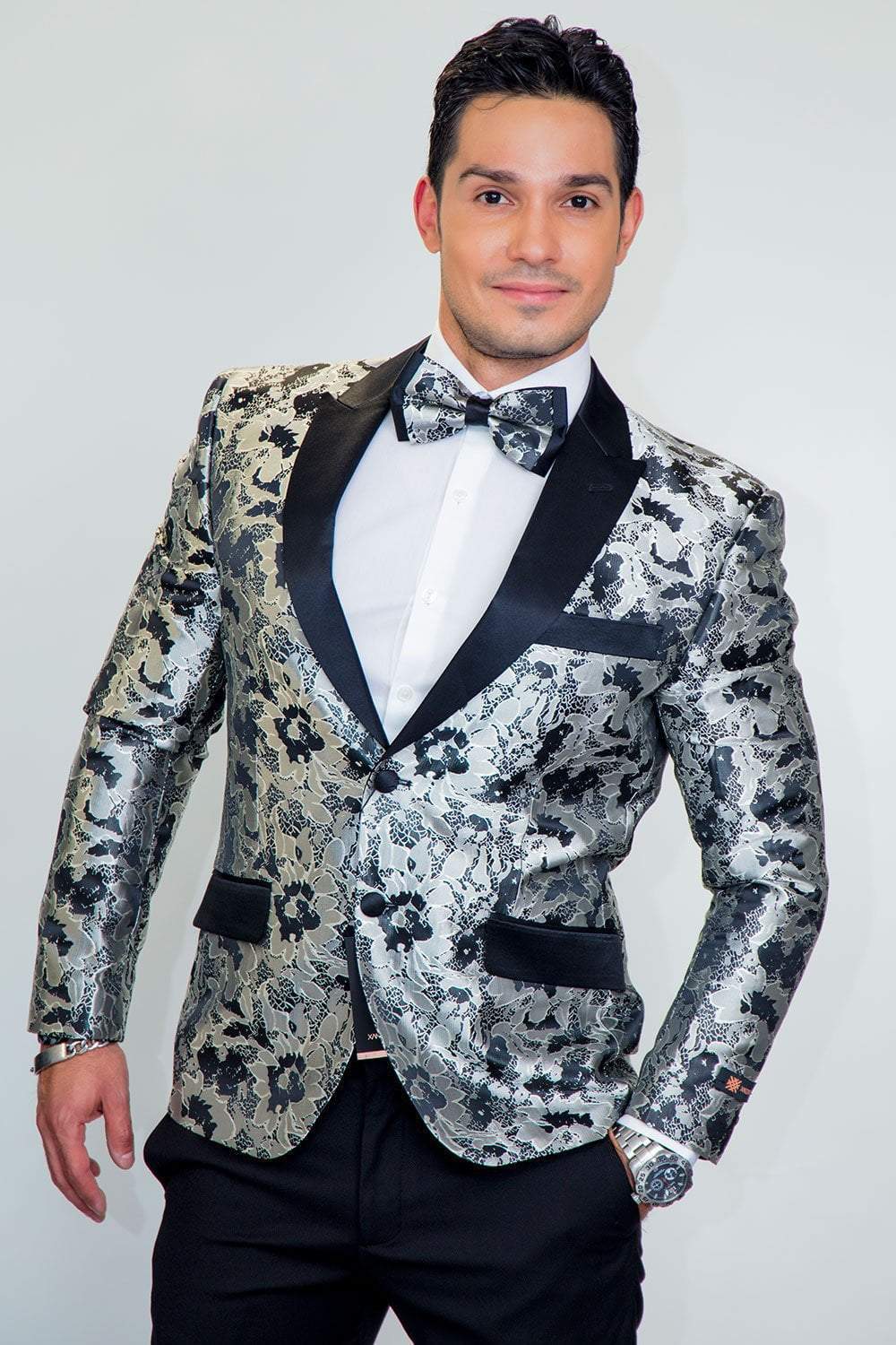 Man wearing Amsterdam Peak tuxedo jacket in metallic silver floral pattern with black lapels and bow tie.
